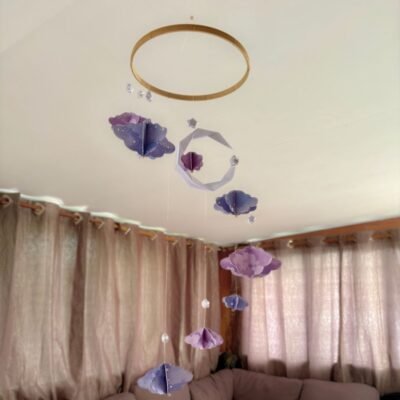 Le mobile Clair de Lune est composé d'un cercle en bambou de 25cm, avec 10 descentes de fil de nylon. Au centre du mobile une lune blanche plié en origami. Autour du cercle les fils sont disposés de sortes à crées une descente progressive de chaque éléments. Sur chaque fil se trouve une étoile blanche en origami, suivi d'un nuage formé à partir de 6 découpe de nuage. Il y a trois tailles de nuage, petit, moyen, grand qui se succèdent. . Les nuages sont mauves avec des motifs léger d'étoiles et de nuages. Ce mobile doux rappellent le début de nuit où les nuages prends une couleur mauve.