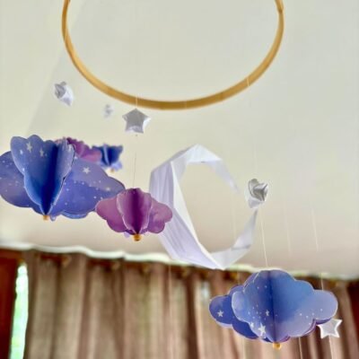 Le mobile Clair de Lune est composé d'un cercle en bambou de 25cm, avec 10 descentes de fil de nylon. Au centre du mobile une lune blanche plié en origami. Autour du cercle les fils sont disposés de sortes à crées une descente progressive de chaque éléments. Sur chaque fil se trouve une étoile blanche en origami, suivi d'un nuage formé à partir de 6 découpe de nuage. Il y a trois tailles de nuage, petit, moyen, grand qui se succèdent. . Les nuages sont mauves avec des motifs léger d'étoiles et de nuages. Ce mobile doux rappellent le début de nuit où les nuages prends une couleur mauve.