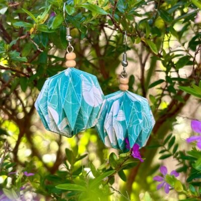 Des boucles d'oreilles avec des crochets simples en acier inoxydable, composées de deux petites perles en bois et d'un pliage en origami qui rappelle la forme des lanternes japonaise ronde ou d'une perle. Ces boucles d'oreilles sont bleues avec des motifs de lotus blancs.