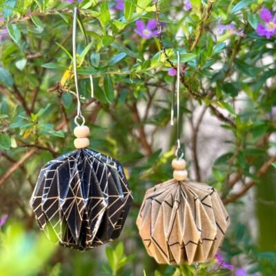 Des boucles d'oreilles avec de longs crochets en acier inoxydable, composées de deux petites perles en bois et d'un pliage en origami qui rappelle la forme des lanternes japonaise ronde ou d'une perle. Ces boucles d'oreilles sont en couleurs dépareillées : d'un côté du marron avec des motifs géométriques noirs et de l'autre du noir avec des motifs géométriques marrons.