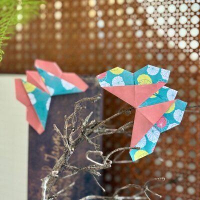 Deux marques pages en forme de papillons, qui se posent dans l'angle du livre. Les deux faces du papier apparaissent et sont inversé sur les deux papillons, soient du rose sans motif et du bleu avec des motifs de feuilles de lotus blanc, rose et jaune.