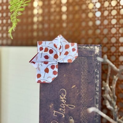 Un marque page en forme de lotus qui se pose dans l'angle du livre, de couleur blanc avec des motifs de feuilles orangées.