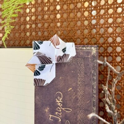 Un marque page en forme de lotus qui se pose dans l'angle du livre, de couleur blanc, avec feuille gingko marron, dorée, et noir.