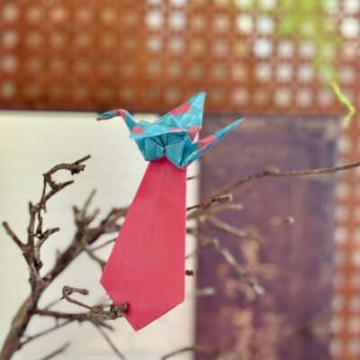 Un marque page de couleur rouge et bleu avec la forme d'une grue. Le marque page se coince entre les pages et laisse dépassé la grue qui se pose sur le haut du livre.