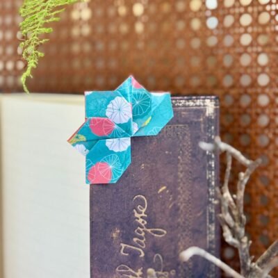 Un marque page en forme de lotus qui se pose dans l'angle du livre, de couleur bleu avec des motifs de feuille de lotus rose, blanc et jaune.