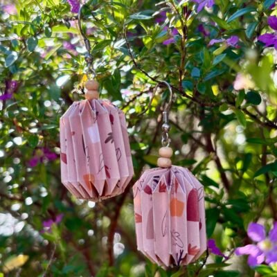 Des boucles d'oreilles avec de longs crochets en acier inoxydable, composées de deux petites perles en bois et d'un pliage en origami qui rappelle la forme des lanternes japonaise. Ces boucles d'oreilles sont beige avec des motifs de feuilles oranges et rouges.