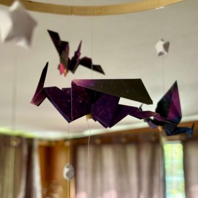 Le mobile dragon est composé d'un cercle en bambou de 25cm, avec 10 descentes de fil de nylon. Le papier utilisé pour les dragons est dans un style galaxie de différente couleur, il est également composé d'étoile en origami appelés "étoile de la chance" de couleur blanche. Au centre du mobile se trouve un gros dragon mauve en dessous de lui un dragon plus petit de couleur verte. Les 9 descentes autour du cercle se déclinent de cette façon : Descente 1 = 1 dragon en haut puis 2 étoiles ; descente 2= 1 étoile, 1 dragon, 1 étoile ; descente 3 = 2 étoiles 1 dragon. Ce modèle est répété sur les 6 autres descentes de façon harmonieuse. Les dragons sont de couleur bleu/verte, rouge/mauve, mauve/bleu. Ce mobile invite à la rêverie, à l'aventure, avec ces dragons majestueux voletant légèrement.
