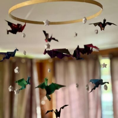 Le mobile dragon est composé d'un cercle en bambou de 25cm, avec 10 descentes de fil de nylon. Le papier utilisé pour les dragons est dans un style galaxie de différente couleur, il est également composé d'étoile en origami appelés "étoile de la chance" de couleur blanche. Au centre du mobile se trouve un gros dragon mauve en dessous de lui un dragon plus petit de couleur verte. Les 9 descentes autour du cercle se déclinent de cette façon : Descente 1 = 1 dragon en haut puis 2 étoiles ; descente 2= 1 étoile, 1 dragon, 1 étoile ; descente 3 = 2 étoiles 1 dragon. Ce modèle est répété sur les 6 autres descentes de façon harmonieuse. Les dragons sont de couleur bleu/verte, rouge/mauve, mauve/bleu. Ce mobile invite à la rêverie, à l'aventure, avec ces dragons majestueux voletant légèrement.