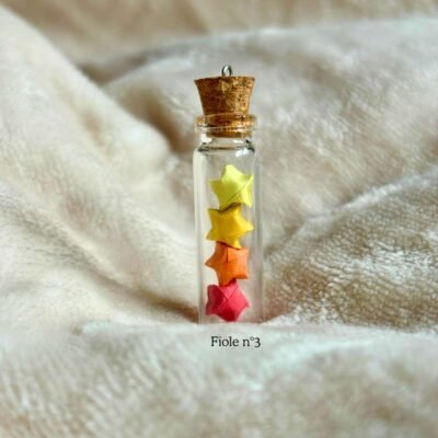 La fiole n°3 est une fiole en verre d'environs 3cm en hauteur et est refermé par un bouchon en liège. La fiole est rempli par 4 minuscule étoiles coloré de 2 nuance de jaunes, orange et rouge. Le bouche en liège contient un petit crochet pour y rajouter un fil au besoin.