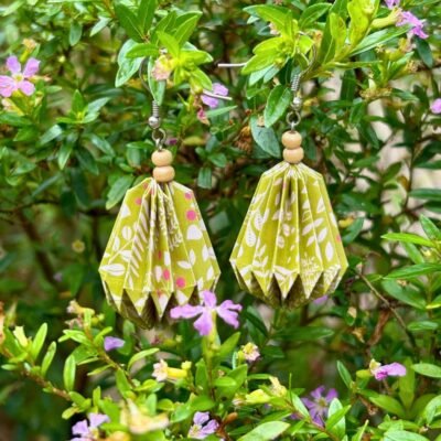 Des boucles d'oreilles avec des crochets simples en acier inoxydable, composées de deux petites perles en bois et d'un pliage en origami qui rappelle la forme d'une goutte d'eau. Ces boucles d'oreilles sont vertes avec des motifs de fleurs blanches.