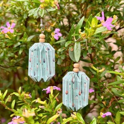 Des boucles d'oreilles avec de longs crochets en acier inoxydable, composées de deux petites perles en bois et d'un pliage en origami qui rappelle la forme des lanternes japonaise. Ces boucles d'oreilles sont bleues clair avec des motifs de flèches.
