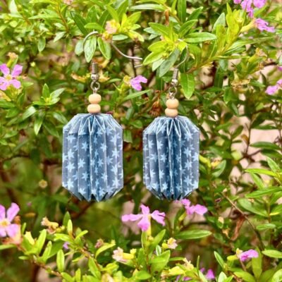 Des boucles d'oreilles avec de longs crochets en acier inoxydable, composées de deux petites perles en bois et d'un pliage en origami qui rappelle la forme des lanternes japonaise. Ces boucles d'oreilles sont bleues foncées avec des étoiles bleues claires.