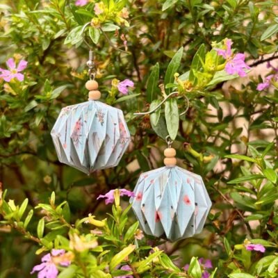 Des boucles d'oreilles avec des crochets simples en acier inoxydable, composées de deux petites perles en bois et d'un pliage en origami qui rappelle la forme des lanternes japonaise ronde ou d'une perle. Ces boucles d'oreilles sont bleues claires avec des motifs type bohème.