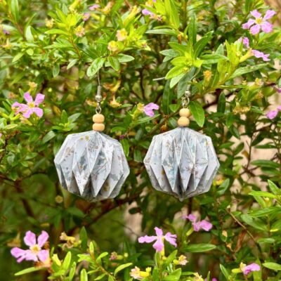 Des boucles d'oreilles avec des crochets simples en acier inoxydable, composées de deux petites perles en bois et d'un pliage en origami qui rappelle la forme des lanternes japonaise ronde ou d'une perle. Ces boucles d'oreilles sont grises avec des motifs type hivernal.