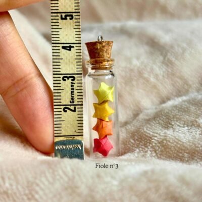 La fiole n°3 est une fiole en verre d'environs 3cm en hauteur et est refermé par un bouchon en liège. La fiole est rempli par 4 minuscule étoiles coloré de 2 nuance de jaunes, orange et rouge. Le bouche en liège contient un petit crochet pour y rajouter un fil au besoin.