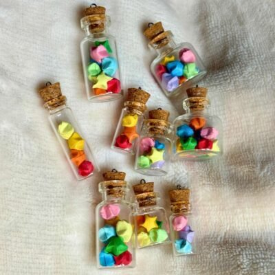 La photo contient des fioles en verre de taille différentes, rempli de minuscules étoiles en origami qu'on appelle étoile de la chance, ces étoiles sont colorés et pliés à la main. Elles sont glissés à l'intérieur des fioles en mélangeant les couleurs.