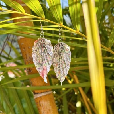 Boucle d'oreille en acier inoxydable argenté, avec un pliage en origami en forme de feuille. Les motifs du papier représentent des fleurs et de attrapes rêves. La couleur dominante est blanche.